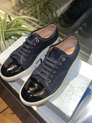 Mörkblå sneakers med lackad tå - Snygga mörkblå sneakers i mocka med svart lackad tå och vita sulor. Skorna har mörkblå snören och metallfärgade öljetter. Perfekta för dig som vill ha en stilren men ändå unik sneaker med cool kontrast mellan mocka och lack. Jätte bra skick, 1 dustbag, extra snören och box ingår 