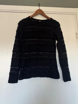 Svart långärmad topp i spets  - Svart långärmad topp med horisontella spetsmönster och tight passform. 