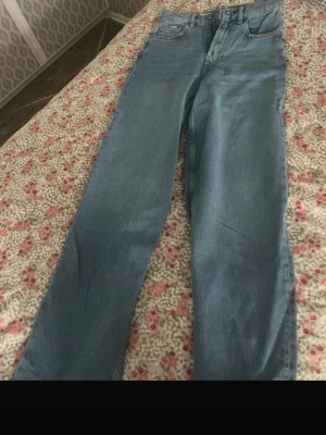 Ljusblå raka jeans - Säljer ett par ljusblå jeans med rak passform och klassisk femficksdesign. Jeansen har hög midja och stängs med dragkedja och knapp. Perfekta för en avslappnad och trendig look.Aldrig använda 