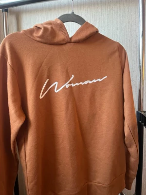 Brun hoodie med vit text - Boohoo hoodie med huva och texten 'Woman' tryckt på framsidan. 