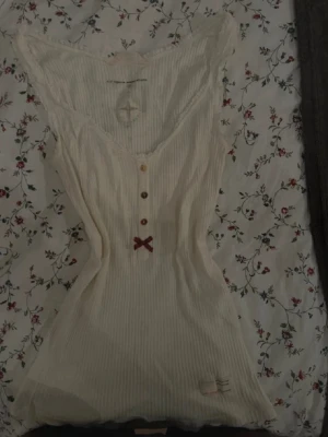 Vitt Odd Molly linne med knappar och rosett  - Storlek: 1 (motsvarar xs-s)  Färg: Vit  Märke: Odd Molly  Utseende: Linne i skönt och tunt material med knappar, spets som följer urringningen med en rosett på   Mycket fint! Kommer ej till användning  