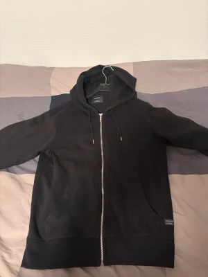 Svart zip hoodie från Jack & Jones - Säljer en svart zip hoodie från Jack & Jones i storlek M. Tröjan är i jättefint skick och har inga skador elller defekter. Knappt använd.
