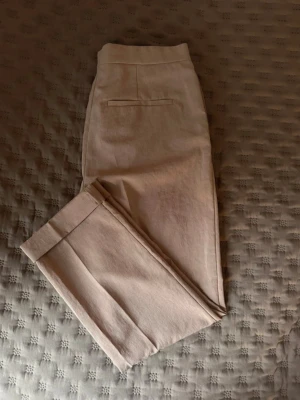Beige kostymbyxa från COS - Stilrena beige kostymbyxor från COS. Byxorna har pressveck och är tillverkade i 100% polyester med foder i bomull. Perfekta för en clean och modern look.