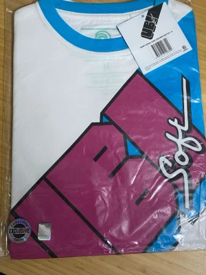 Vit och blå t-shirt  - Cool vit t-shirt från Ubi med blå krage och stort grafiskt tryck i rosa, blått och svart framtill. T-shirten har en klassisk passform och är tillverkad i mjuk bomull, perfekt för en avslappnad streetstyle-look.
