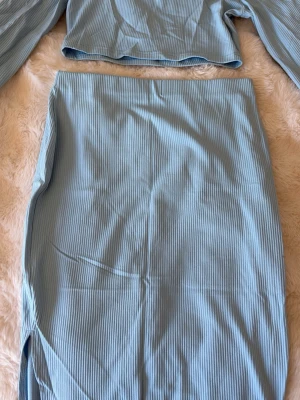 Ljusblått ribbat set med kjol och topp - Säljer ett ljusblått ribbat set med långärmad topp och matchande kjol med slits. Setet är i mjukt, stretchigt tyg och har en enkel, stilren design. Perfekt för dig som gillar en avslappnad men trendig look. Skriv för frågor❤️