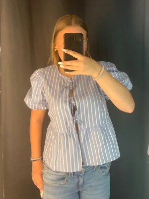 Blåvit randig blus med puffärm - Söt blå blus med vita ränder och puffiga korta ärmar. Har knytningar framtill och lite utsvängd passform!