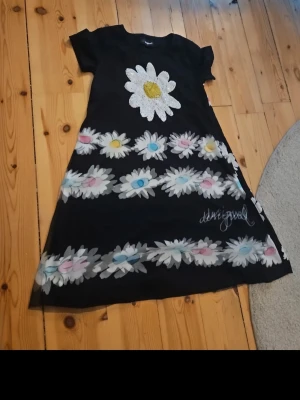 Svart klänning med prästkragar Desigual - Svart klänning från Desigual med färgglada prästkragar i vitt, gult, blått och rosa. Klänningen har korta ärmar och A-linjeformad passform. Perfekt för dig som gillar unika och lekfulla mönster.