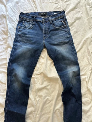 Blå jeans från Replay - Snygga blå jeans från Replay med klassisk femficksdesign och diskreta slitningar framtill. Jeansen har raka ben och detaljerade sömmar, samt logotyp på myntfickan. Perfekta för en avslappnad och trendig look. Storlek 28