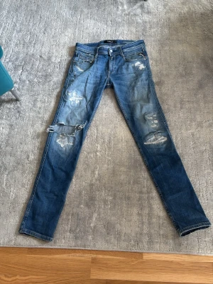 Replay jeans - W28 L32. Snygga blå skinny jeans med slitningar och hål på benen. Jeansen har klassisk femficksdesign, låg midja och dragkedjegylf. Perfekta för en trendig och avslappnad stil. Materialet är denim i bomull.