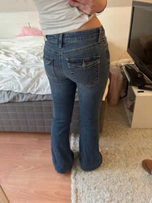 Blå bootcut jeans med fickdetaljer - Snygga blå bootcut jeans med klassiska fickor bak och fram. Jeansen har en lätt utsvängd passform och normalhög midja. Perfekta för dig som gillar en retrostil och vill ha ett par jeans som sticker ut lite extra.