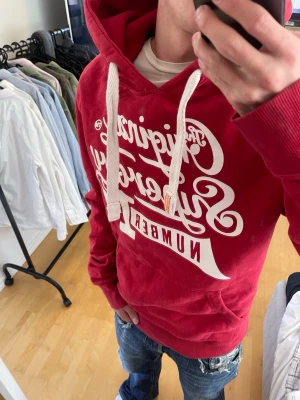Röd Superdry hoodie med tryck - Säljer nu denna sjukt snygga Vintage 2000s SuperDry hoodie! Passar till allt och har en perfekt passform. Säljs ej längre i butik och är därav mycket eftertraktad😊 Skriv vid funderingar 🤝