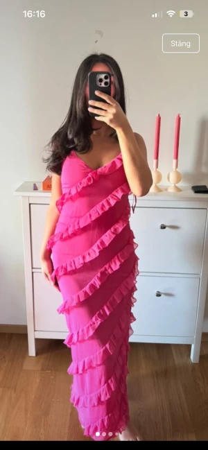Rosa volangklänning med smala axelband - Snygg långklänning i stark rosa med smala axelband och massa fina volanger. Klänningen har en figurnära passform och är perfekt för dig som vill sticka ut. Materialet känns lätt och luftigt. 
