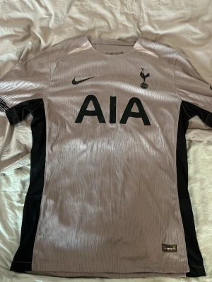 Tottenham Hotspur matchtröja Nike player edition - Säljer en Tottenham Hotspur matchtröja från Nike i ljusgrått med svarta detaljer och klubbens emblem på bröstet. Tröjan har svart Nike-logga, AIA sponsortryck och är tillverkad i ett lätt och ventilerande material perfekt för träning eller match.