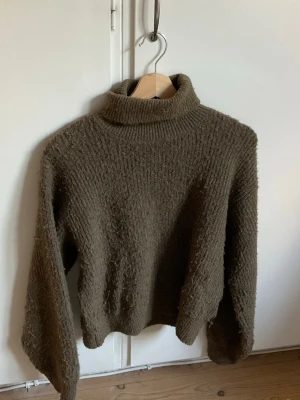 Grön/brun stickad tröja från Zara - Mysig brun stickad polotröja med grov struktur och lång ärm. Tröjan har en hög, ribbstickad krage och avslappnad passform. Perfekt för kalla dagar och enkel att matcha med jeans eller kjol.