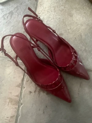 Vinröda lackpumps med remmar - Aldrig använda. Snygga vinröda pumps från Brunate i glansigt lackmaterial. Skorna har spetsig tå, öppen häl och smala justerbara remmar med spänne. 
