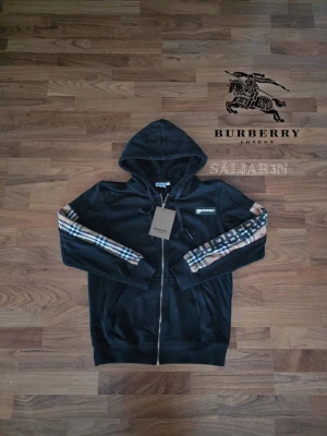 Burberry Hoodie - Burberry Hoodie – Storlek S – Nyskick Exklusiv svart Burberry-hoodie i nyskick, storlek S. Huvtröjan har ikoniska Burberry-rutor längs ärmarna och stor logotyp, samt diskret Burberry-emblem på bröstet. Zippen är märkessignerad med Burberry. Praktiska fickor fram och dragkedja gör den både funktionell och stilren. Perfekt för vardag eller trendig streetwear. 📦 Snabb leverans – skickas samma dag (om ej hindr.) 📩 Kontakta vid frågor.