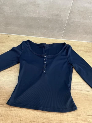 Mörkblå ribbad topp med knappar - Mörkblå långärmad ribbad topp med rund halsringning och knappdetaljer framtill. Snygg och enkel modell som passar till mycket. Materialet är stretchigt och följsamt.