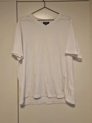 Vit v-ringad t-shirt från SMOG  - Klassisk vit t-shirt från SMOG med v-ringning och korta ärmar. Tillverkad i mjuk bomull och har en avslappnad passform som passar perfekt till jeans eller shorts.