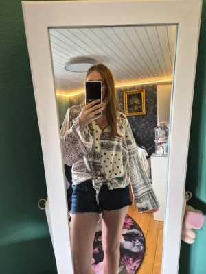 Mönstrad blus från Rut&Circle - Snygg vit blus från Rut&Circle med svart paisleymönster och prickar. Blusen har lång ärm, v-ringning och knytdetalj framtill. Perfekt för en trendig och avslappnad look.