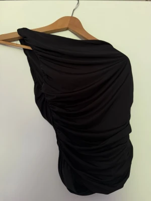 Svart one shoulder draperad klänning - Säljer denna snygga one shoulder toppen som är lite tightare i midjan från bikbok. Har använts 1 gång. 