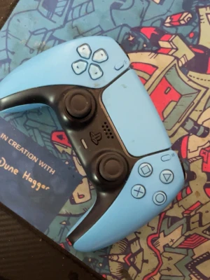 Blå PlayStation 5 DualSense handkontroll - Snygg blå PlayStation 5 DualSense handkontroll från Sony. Knappt använt den Ergonomisk design med svarta detaljer och klassiska PlayStation-knappar. Tillverkad i plast med greppvänlig form och inbyggd touchpad. Perfekt för gaming på PS5.