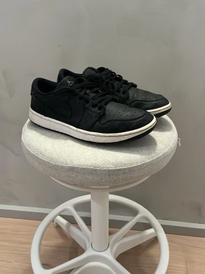 Svarta Air Jordan 1 Low Golf sneakers - Svarta Air Jordan 1 Low Golf med läderöverdel, perforerad tåbox och klassisk vit yttersula. Skorna har svarta skosnören, diskret Swoosh på sidan och Jordan-logga på plösen. Snygg och sportig modell för dig som gillar streetwear och golf. Små i storlek, använda runt 5 gånger. Nypris 1899