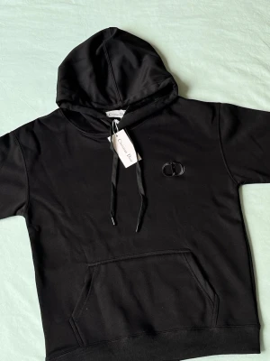 Svart hoodie från Christian Dior - Snygg svart hoodie från Christian Dior med broderad CD-logga på bröstet. Klassisk känguruficka framtill, justerbar dragsko i huvan och ribbade muddar. Perfekt för dig som vill ha en stilren och exklusiv look.