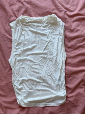 Vit ärmlös linnetopp - En basic vit ärmlös linnetopp i mjukt material. Toppen har en enkel och rak passform med rundad halsringning. Perfekt att styla till jeans eller kjol för en clean look.