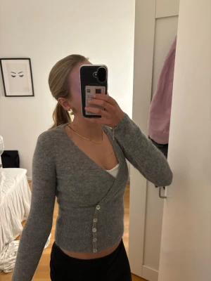 Grå alpaca blend tröja från Gina tricot - Snygg grå omlottkofta med v-ringning och pärlemorknappar framtill. Koftan är figurnära med ribbad midja och långa ärmar. Perfekt att styla över ett linne eller topp för en chill men trendig look.skriv för fler bilder eller diskutera pris💕