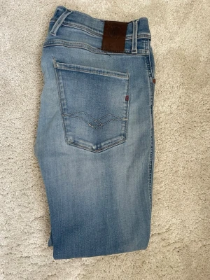 Replay anbass - Snygga ljusblå jeans från Guess i slim fit-modell. Jeansen har klassisk femficksdesign, diskreta slitningar och logotyppatch i läder baktill. Tillverkade i mjuk denim med stretch för extra komfort. Perfekta för en trendig och avslappnad stil.