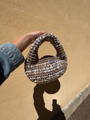 Beige chunky virkad axelväska - Modell ANKI - Glitter confetti - Superfin axelväska i chunky virkat material med beige och bruna toner. Väskan har en rundad form och ett brett handtag som gör den både snygg och bekväm att bära.