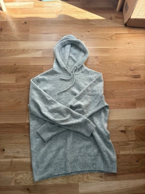 Ljusgrå hoodie i mjuk ullmix - Snygg ljusgrå hoodie med huva och dragsko. Tillverkad i en mjuk och skön ullmix som känns lyxig mot huden. Långa ärmar och ribbade muddar vid ärmslut och nederkant. Perfekt för en avslappnad och stilren look.