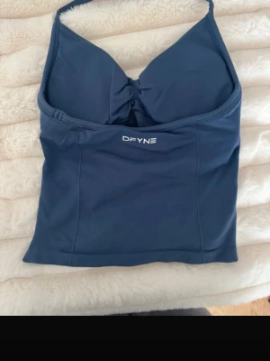 Blå linnetopp från DFYNE - Snygg blå linnetopp från DFYNE med smala axelband och twistad detalj framtill. Toppen har en sportig look och är tillverkad i ett stretchigt syntetmaterial som passar perfekt till träning eller en aktiv vardag.