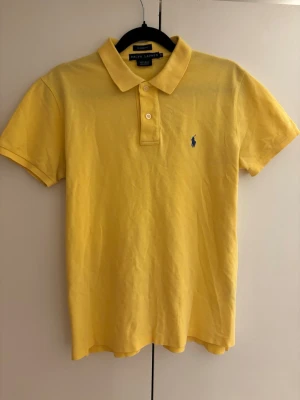 Ralph Lauren Classic Fit polo - Helt oanvänd Ralph Lauren pikétröja i gult med blå logga. Classic Fit-modell. Inga fläckar eller defekter, i nyskick.                      Stl M