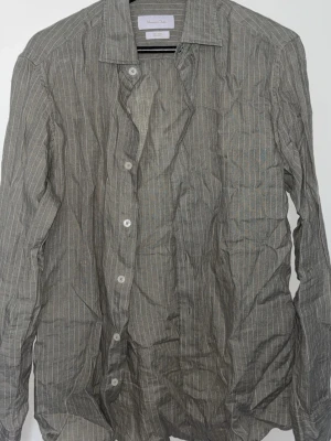 Grå randig skjorta från Massimo dutti - Klassisk grå skjorta från Oscar Jacobson med tunna vita ränder. Skjortan har lång ärm, knappar framtill och en avslappnad krage. Tillverkad i bomull för en skön känsla och stilren look.