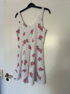 Kort blommig klänning - Blommig klänning. Tyget är lite genomskinligt. Finns några få skavanker (se bilder), men inget som påverkar. Endast använd några få gånger. 