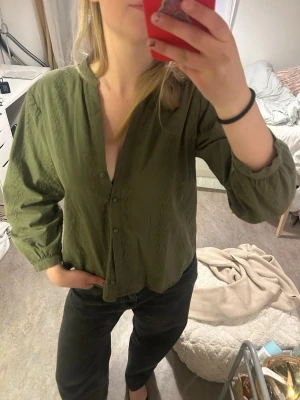 Olivgrön blus med knappar - Snygg olivgrön blus med knappar framtill och diskreta broderade detaljer längs framsidan. Blusen har en avslappnad passform, V-ringning och långa ärmar med lätt puff vid axlarna. Perfekt att styla till både jeans och kjol.😎 