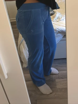Blå velourbyxor Juicy Couture - Snygga blå mjukisbyxor från Juicy Couture i mjuk velour. Byxorna har raka ben, resår och dragsko i midjan samt fickor fram och bak. Perfekta för en chill och trendig look.