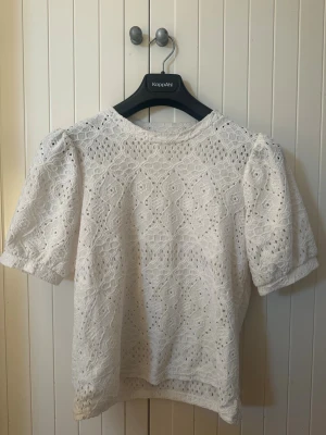 Topp  - Söt vit topp från Object i broderad spets med puffärmar och rund hals. Blusen har ett romantiskt mönster och är tillverkad i ett lätt, luftigt material som passar perfekt till jeans eller kjol. 🤍