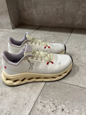 On Running vita sneakers med beige sula - Snygga sneakers från On Running i vitt med beige chunky sula och röda detaljer på snörningen. Ovandelen är i mesh för bra andningsförmåga och komfort. Perfekta för dig som gillar stilrena och moderna skor med unik design.