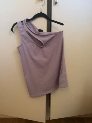 Ljuslila oneshoulder ribbad topp - Trendig ljuslila oneshoulder topp med ribbad struktur och unik asymmetrisk axelrem. Perfekt för dig som vill sticka ut med en cool och modern look. Materialet känns mjukt och följsamt mot huden.