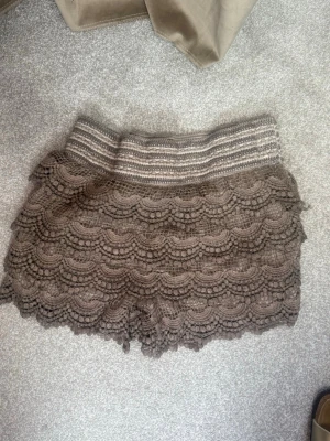 Bruna virkade shorts med volang - Säljer ett par bruna virkade shorts med bred resår i midjan och flera lager volangdetaljer. Shortsen har en bohemisk vibe och är perfekta för sommardagar. De är mjuka och stretchiga för extra komfort.