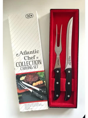 Atlantic Chef trancherset i presentask - kniv och gaffel - Stilrent trancher-set / grillbestick från Atlantic Chef. Setet innehåller en kniv och en gaffel. Bladen är tillverkade av rostfritt stål med högt kolinnehåll. Handtagen är tillverkade av svart fenol- och träblandning. Full tånge med två nitar av speciallegerat stål. Säkerhetsgrepp. Tål maskindisk. Levereras i originalförpackning. Kartongen har sett bättre dar, men besticken är helt nya!