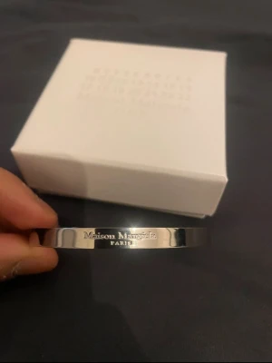 Maison Margiela silverarmband - Snyggt och stilrent armband från Maison Margiela i silver. Öppen design som gör det enkelt att ta på och av. Märkets logotyp är ingraverad på framsidan för en exklusiv touch. Perfekt accessoar för dig som gillar minimalistisk och modern stil.