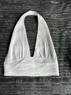 Vit ribbad halterneck topp - Säljer en vit halterneck topp med ribbad struktur och bred kant under bysten. Toppen är ärmlös och har en djup v-ringning framtill. Perfekt för dig som gillar en stilren och trendig look. Har ingen aning va den kommer ifrån för kommer ej ihåg.. o tyvärr klippt bort lapparna…