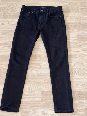 Svarta nudie jeans - Snygga svarta slim fit jeans från Nudie Jeans med klassisk femficksdesign och diskreta nitar. Jeansen har en rak passform och är tillverkade i stretchigt bomullsmaterial för extra komfort. Perfekta för en stilren och modern look. Skick 9/10 knappt använda. Kan gå ner i pris vid snabba affärer.
