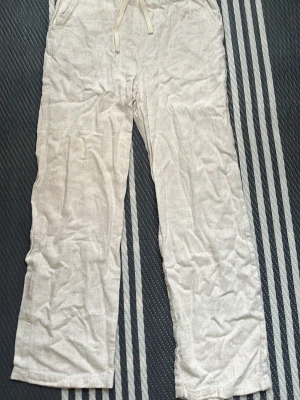 Beiga linnebyxor från Grunt - Säljer ett par beiga linnebyxor från Grunt i storlek M barn. Byxorna har raka ben, dragsko i midjan och sidofickor. Perfekta för en avslappnad och stilren look. Materialet är luftigt och passar bra till varmare dagar.