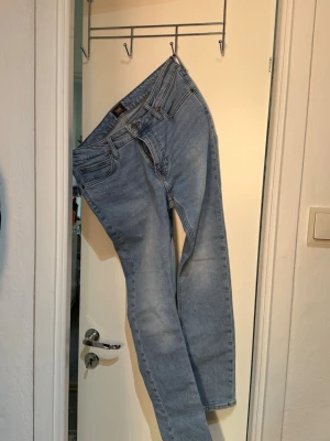 Ljusblå Lee jeans med rak passform - Säljer ett par ljusblå jeans från Lee med klassisk rak passform och fem fickor. Jeansen har bälteshällor, dragkedjegylf och Lee-logga på knapp och etikett. Perfekta för en avslappnad och trendig look.