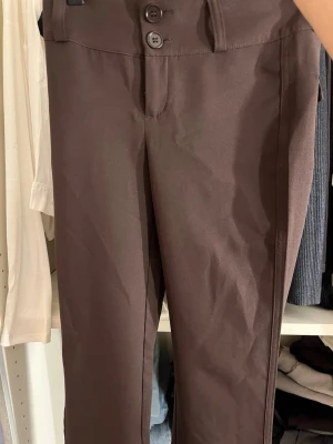 Bruna bootcut kostymbyxor gina tricot - Mörkbruna kostymbyxor i bootcut-modell med två knappar framtill och fickor med lock och knapp bak. Snygg passform och klassisk look, perfekta för en trendig och stilren outfit. Från Gina tricot, har kvar prislapp 
