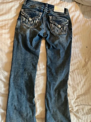 Blå bootcut jeans med broderade fickor - Säljer mina favvo blå bootcut jeans med snygga broderade detaljer och dekorationer på bakfickorna💗. Jeansen är köpta i USA och passar till alla typer av kläder. Tillverkade i denim med lätt tvättad look. Perfekta för dig som gillar en avslappnad men trendig stil.